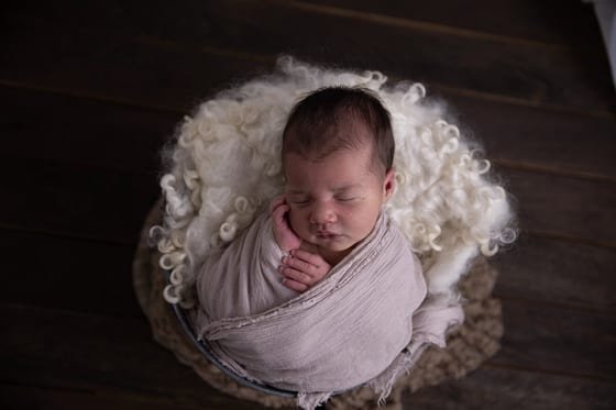 Wrapped newborn in a fur-lined bowl — before retouching