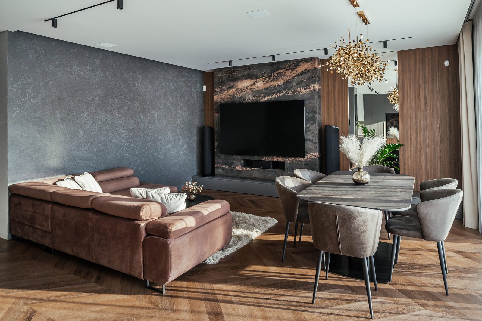Svetainė su rudos odos sofa, valgomojo stalu ir auksiniu šviestuvu