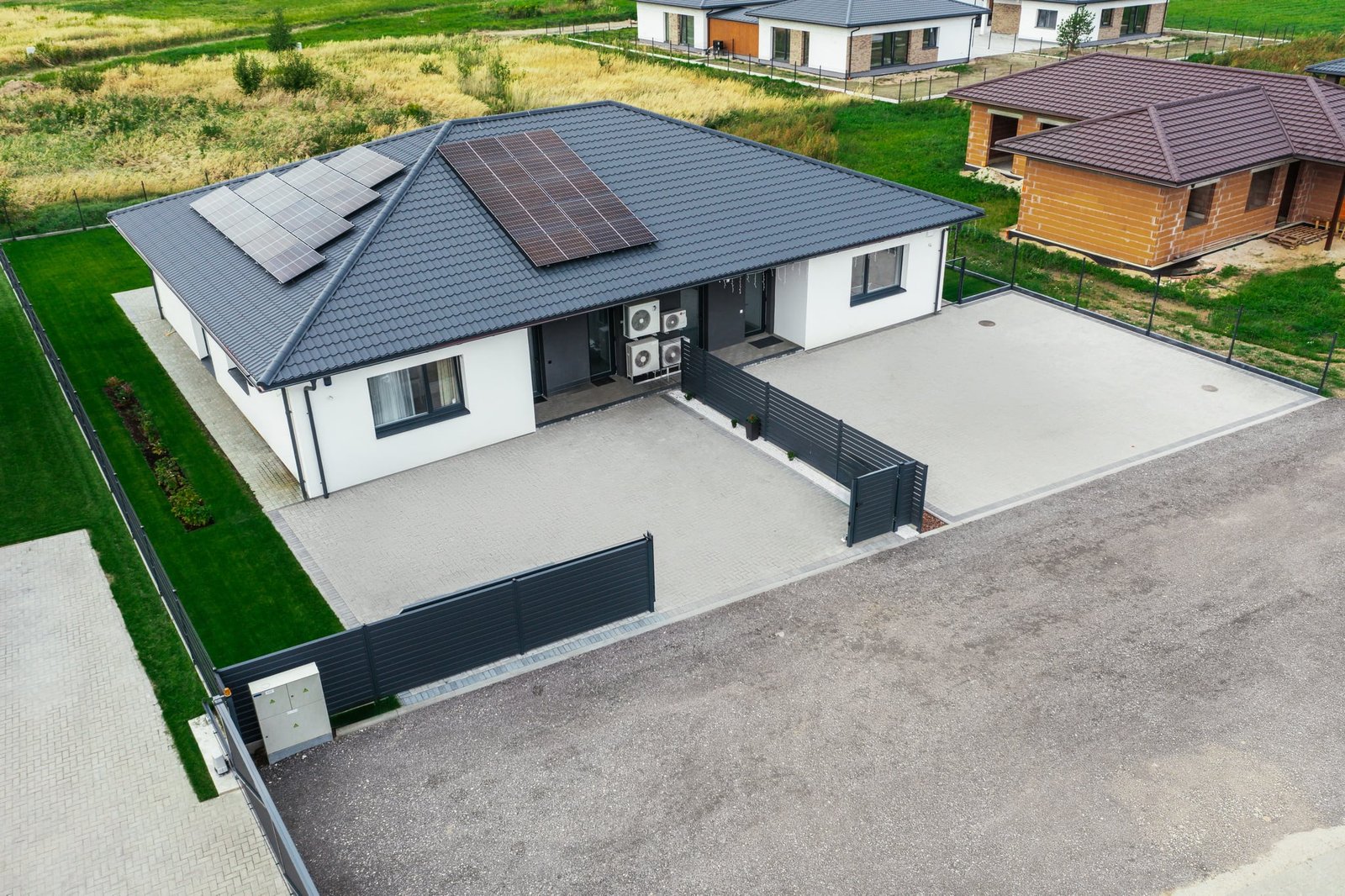 Kotedžų kvartalas iš drono: du namai su saulės moduliais ant stogo ir trinkelėmis grįstais kiemais — po retušo